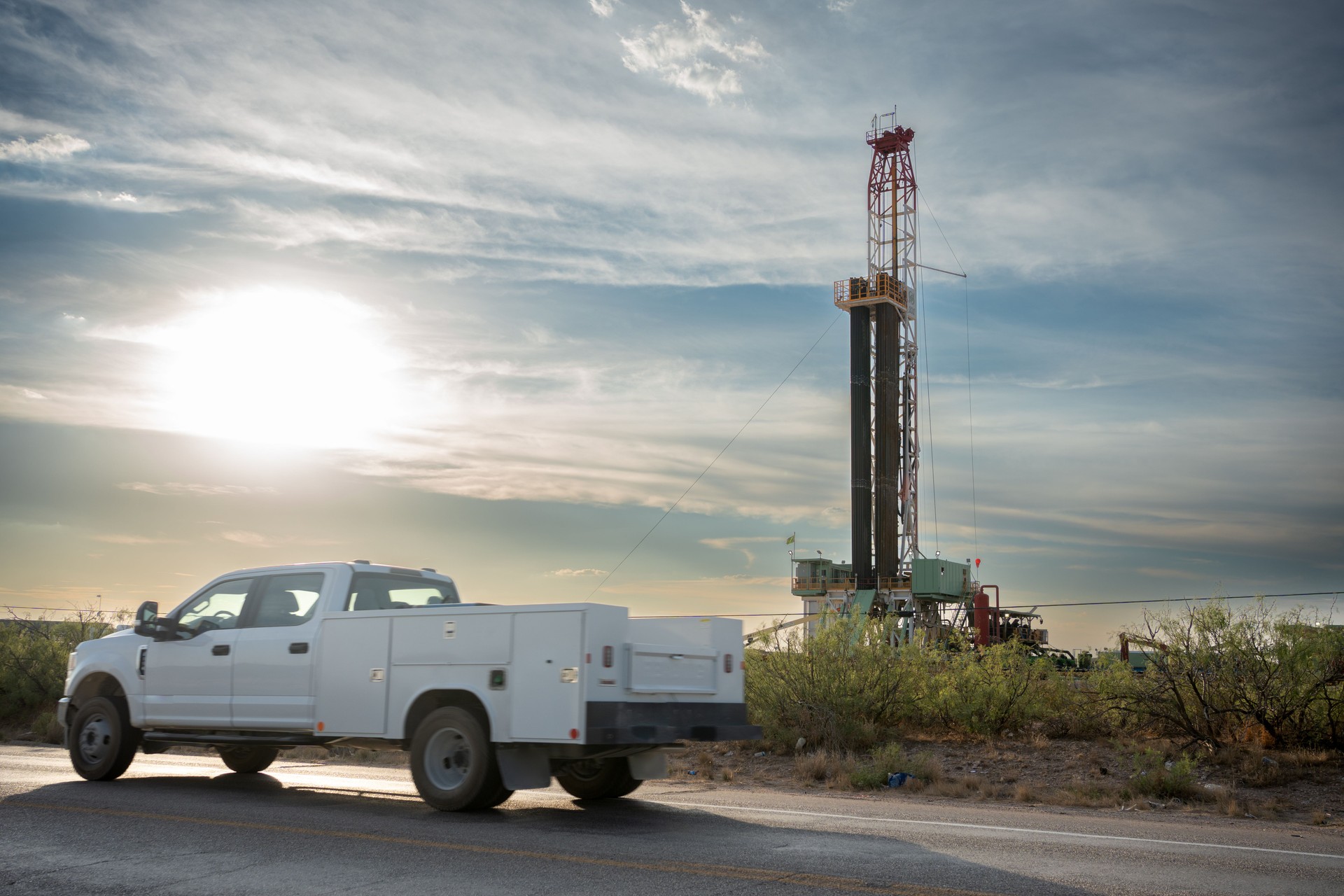 Truck passes by an oil drilling platform with a fracking rig in operation, extracting fuel to meet the world's demands